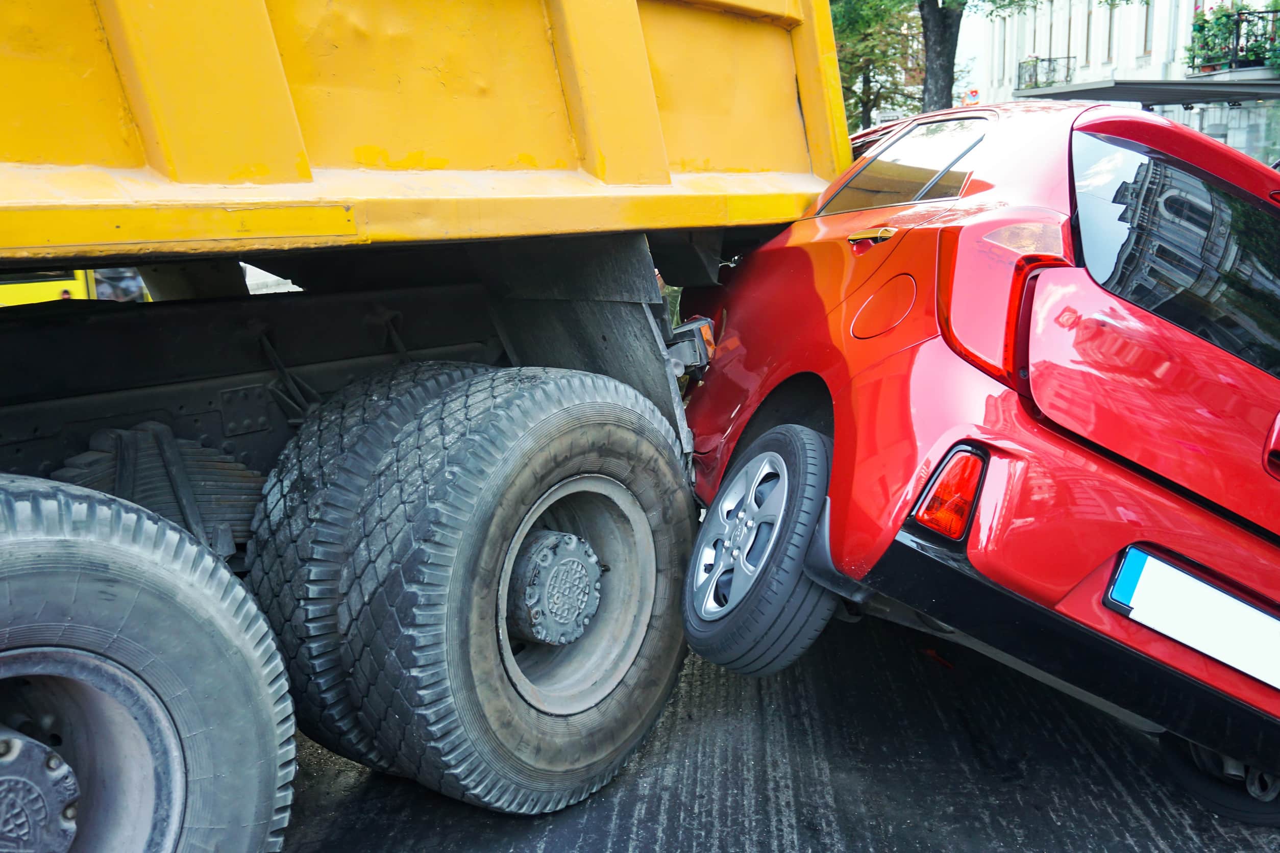 Red passenger car lodged beneath the rear of a large commercial truck after a serious collision, illustrating the devastating impact of truck accidents and the importance of understanding Texas truck accident laws.
